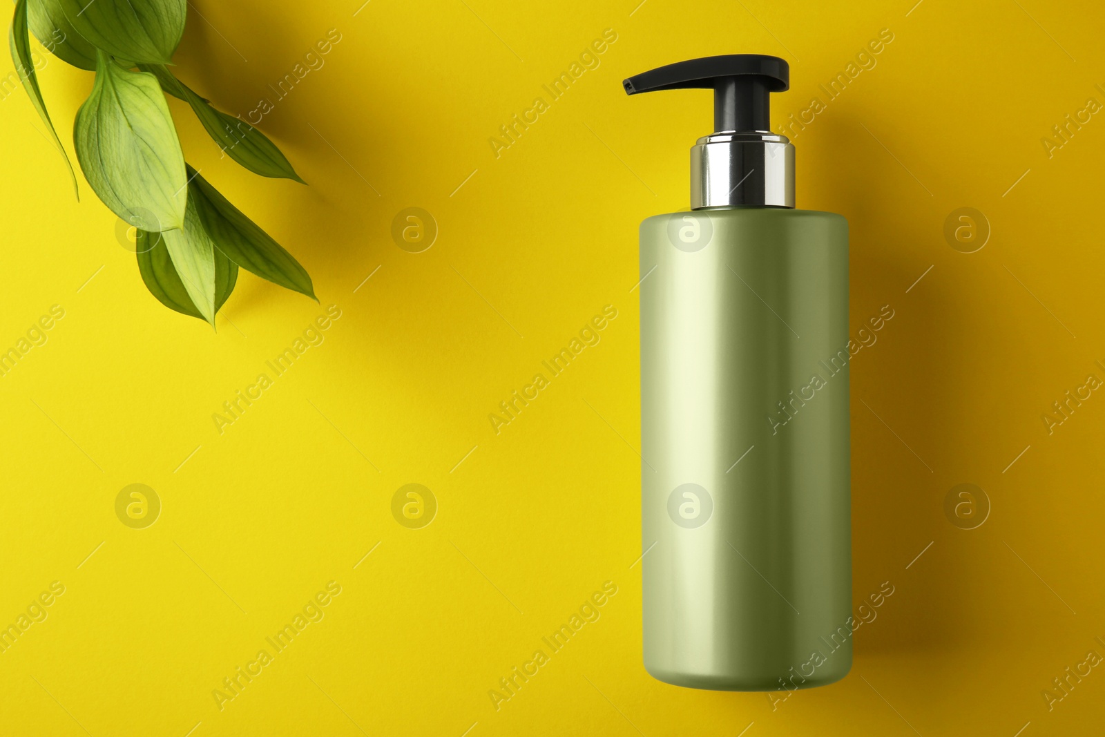 Photo of Bottle of shampoo and green leaves on yellow background, flat lay. Space for text