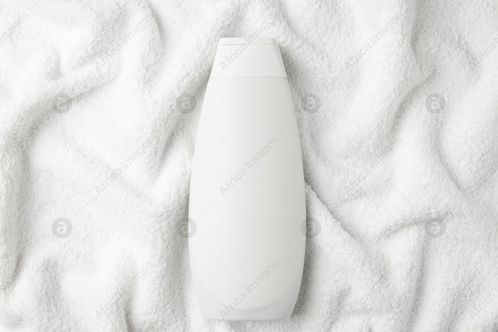 Photo of Bottle of shampoo on soft terry towel, top view