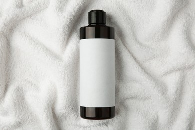 Photo of Bottle of shampoo on soft terry towel, top view