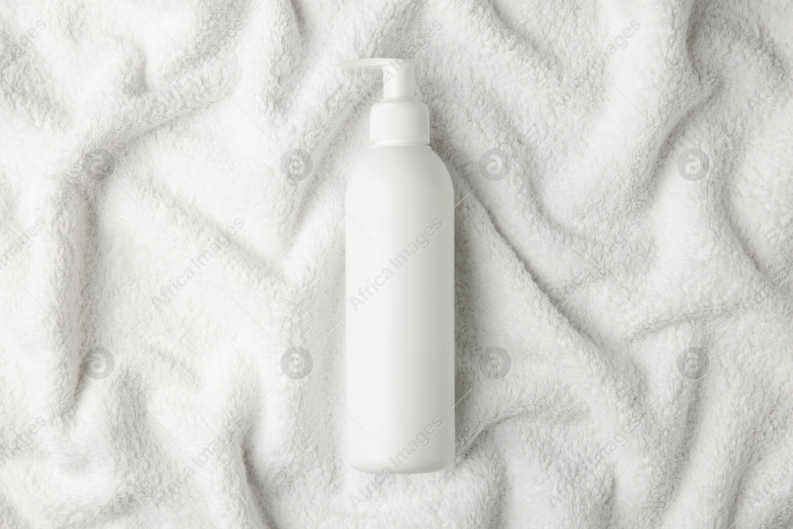 Photo of Bottle of shampoo on soft terry towel, top view