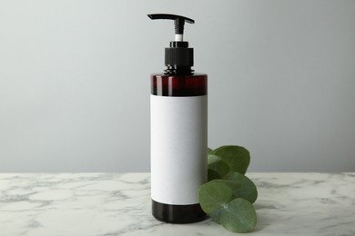 Photo of Bottle of shampoo and eucalyptus branch on white marble table against grey background