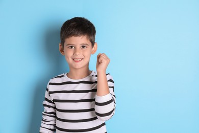 Portrait of cute little boy on light blue background, space for text