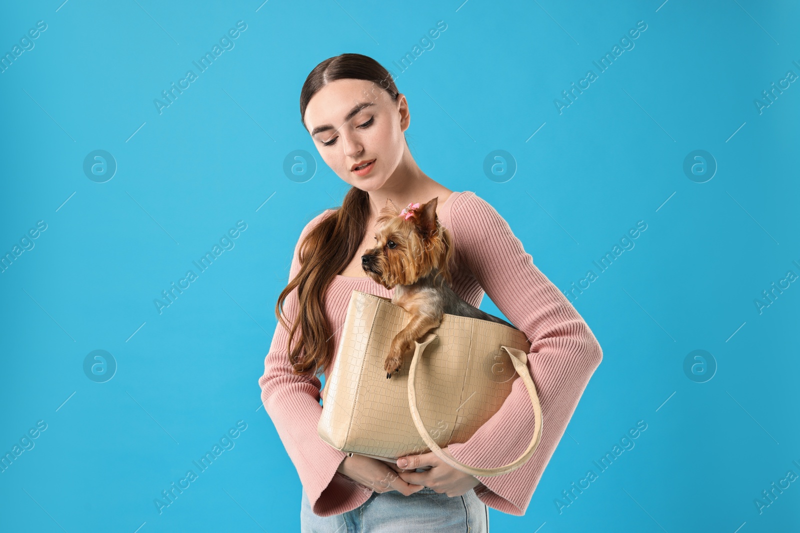 Photo of Beautiful young woman holding bag with cute Yorkshire Terrier dog on light blue background