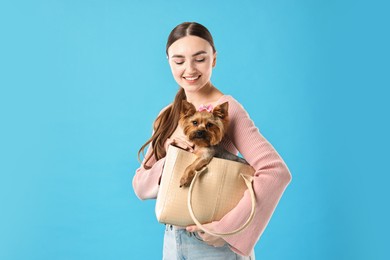 Photo of Beautiful young woman holding bag with cute Yorkshire Terrier dog on light blue background