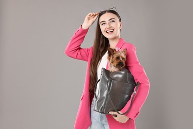 Beautiful young woman carrying cute Yorkshire Terrier dog in bag on grey background