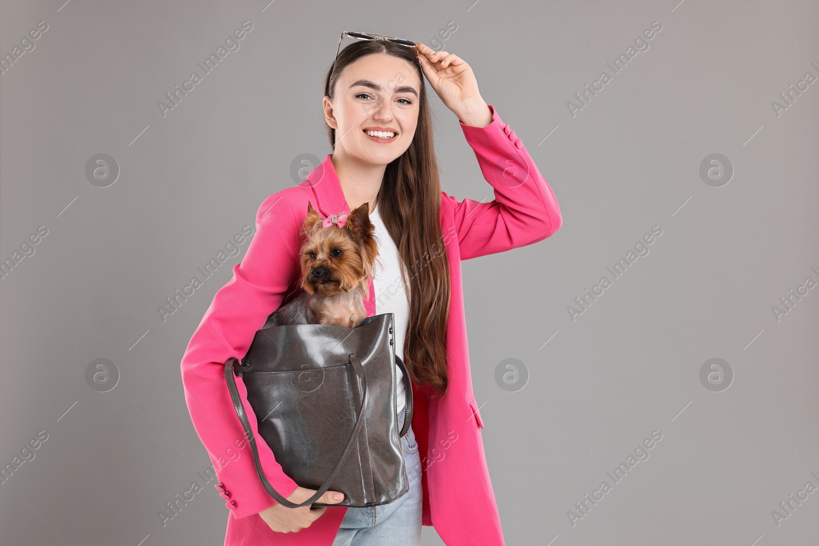 Photo of Beautiful young woman carrying cute Yorkshire Terrier dog in bag on grey background