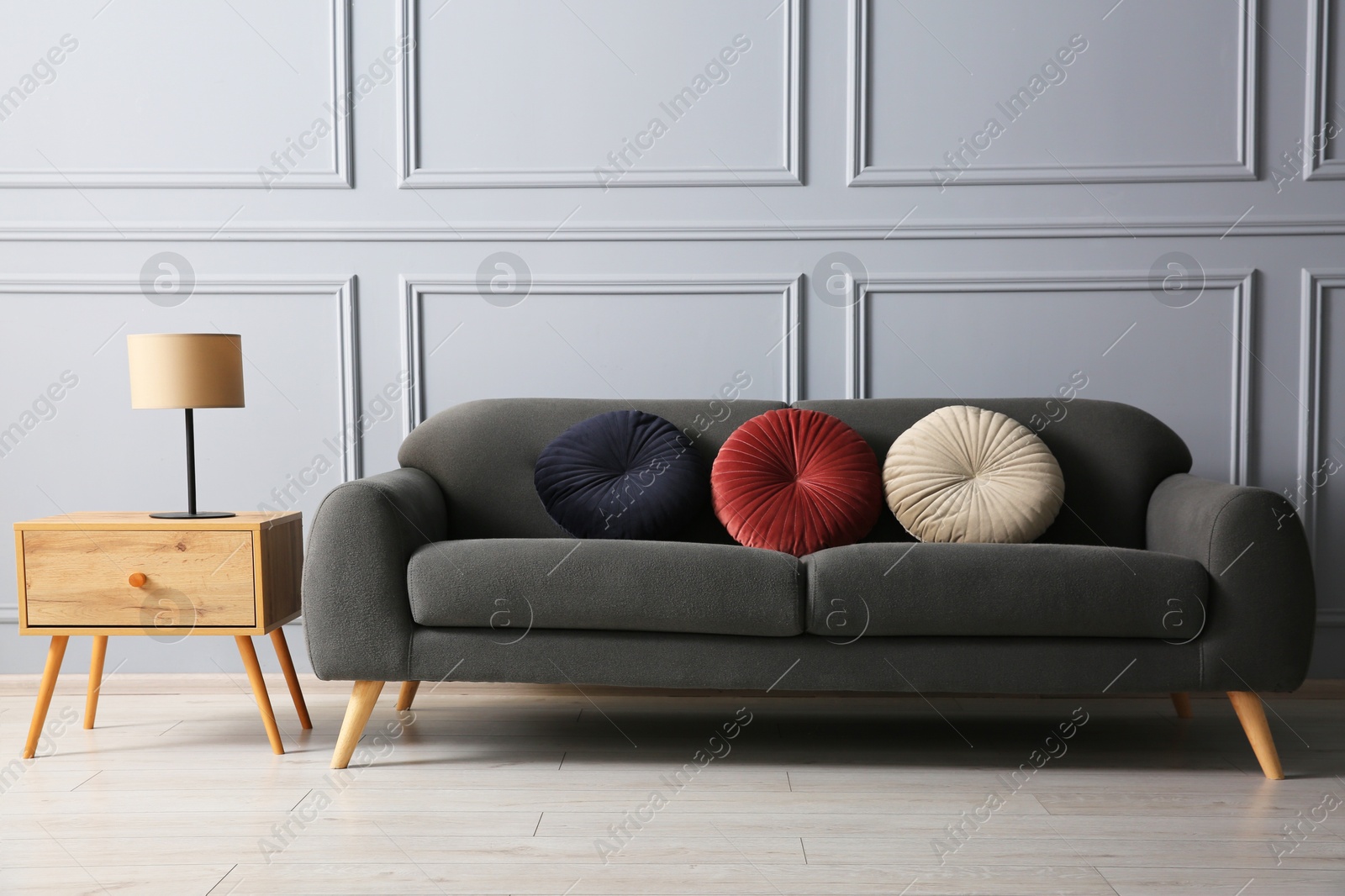 Photo of Stylish sofa with cushions and lamp on side table near grey wall