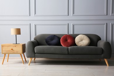 Stylish sofa with cushions and lamp on side table near grey wall