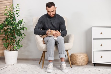 Photo of Man petting cute ginger cat on armchair at home