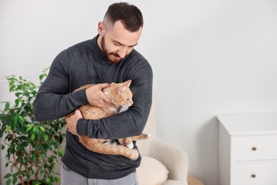 Photo of Man petting cute ginger cat at home, space for text