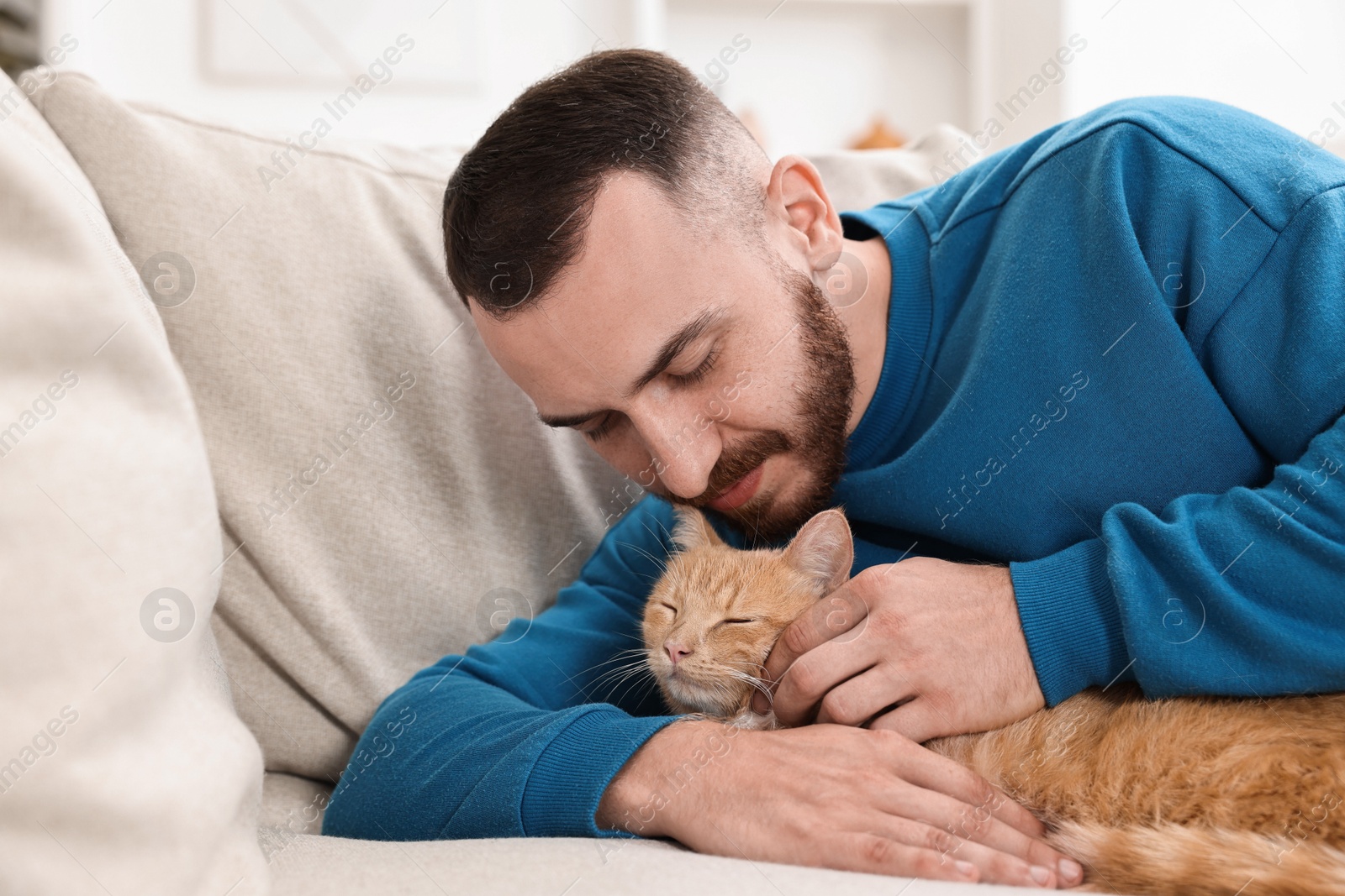 Photo of Man petting cute ginger cat on sofa at home