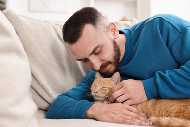 Photo of Man petting cute ginger cat on sofa at home