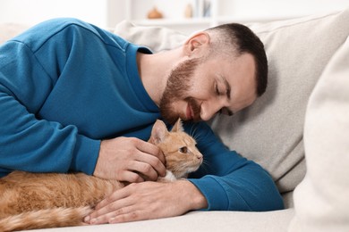 Photo of Man petting cute ginger cat on sofa at home