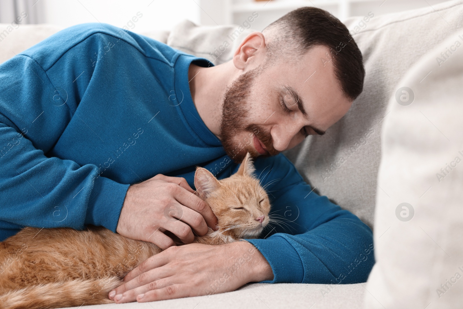 Photo of Man petting cute ginger cat on sofa at home