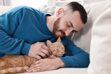 Photo of Man petting cute ginger cat on sofa at home