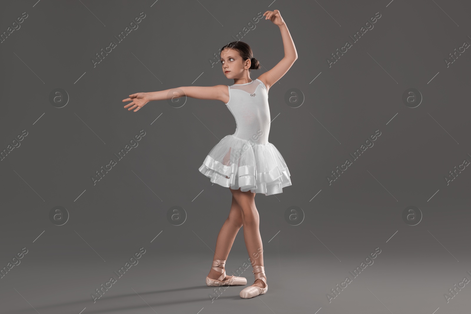 Photo of Cute little ballerina dancing on grey background