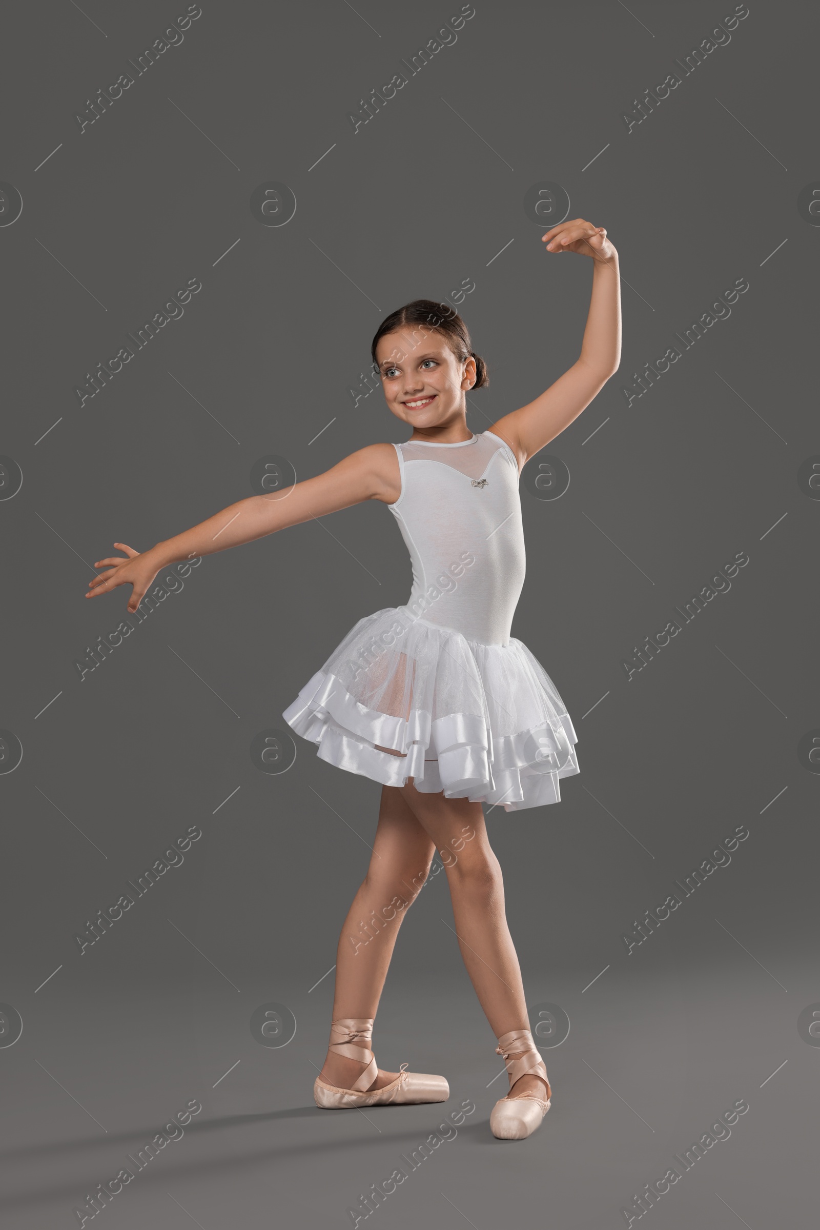 Photo of Cute little ballerina dancing on grey background