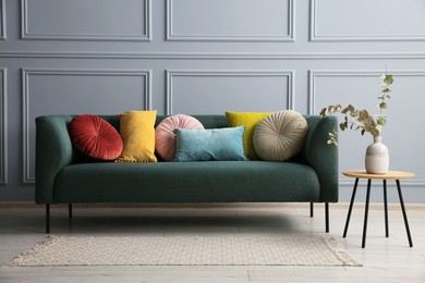 Stylish sofa with cushions and eucalyptus branches in vase on side table near grey wall