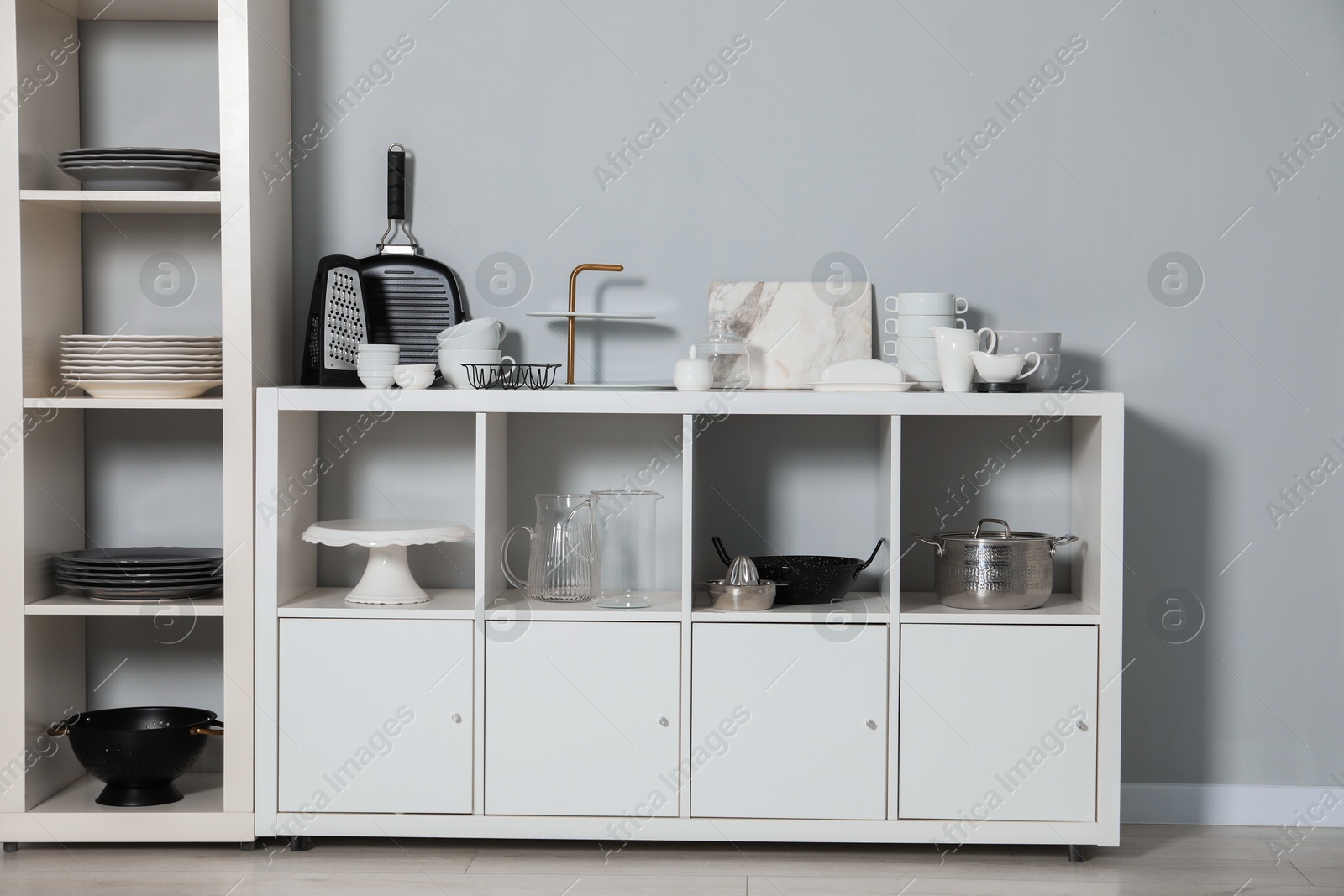 Photo of Shelving unit and storage cabinet with kitchenware near grey wall indoors