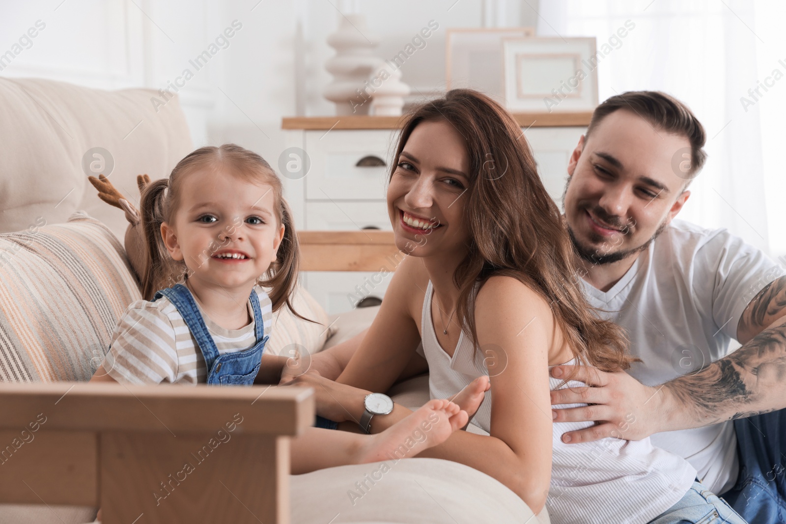 Photo of Happy family. Parents and their cute little daughter on sofa at home