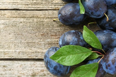 Photo of Tasty ripe plums and leaves on wooden table, flat lay. Space for text