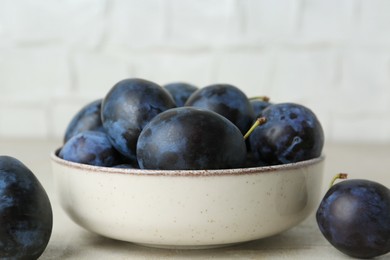 Photo of Ripe plums in bowl on light table, closeup