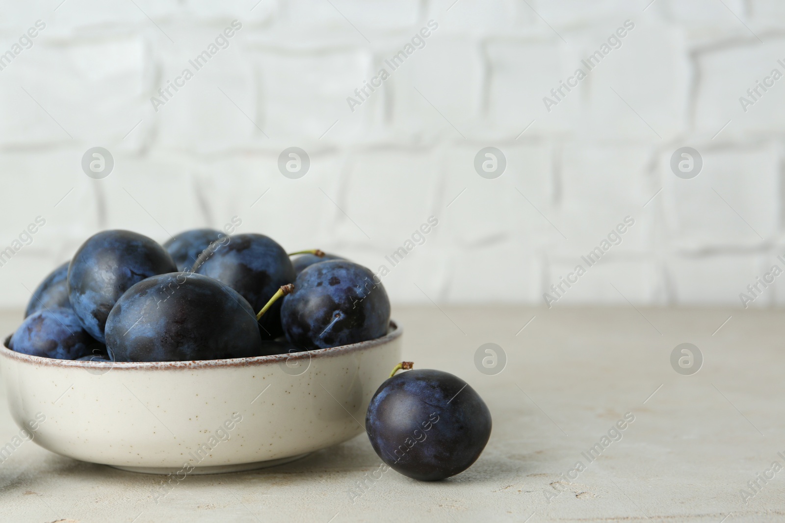 Photo of Ripe plums in bowl on light textured table, space for text