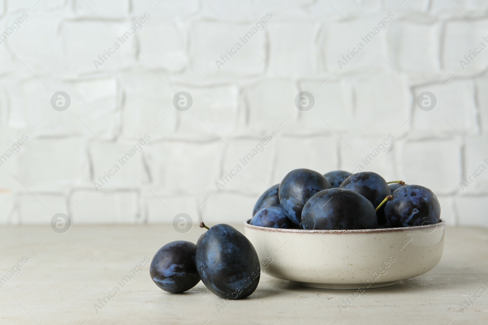 Photo of Ripe plums in bowl on light textured table, space for text