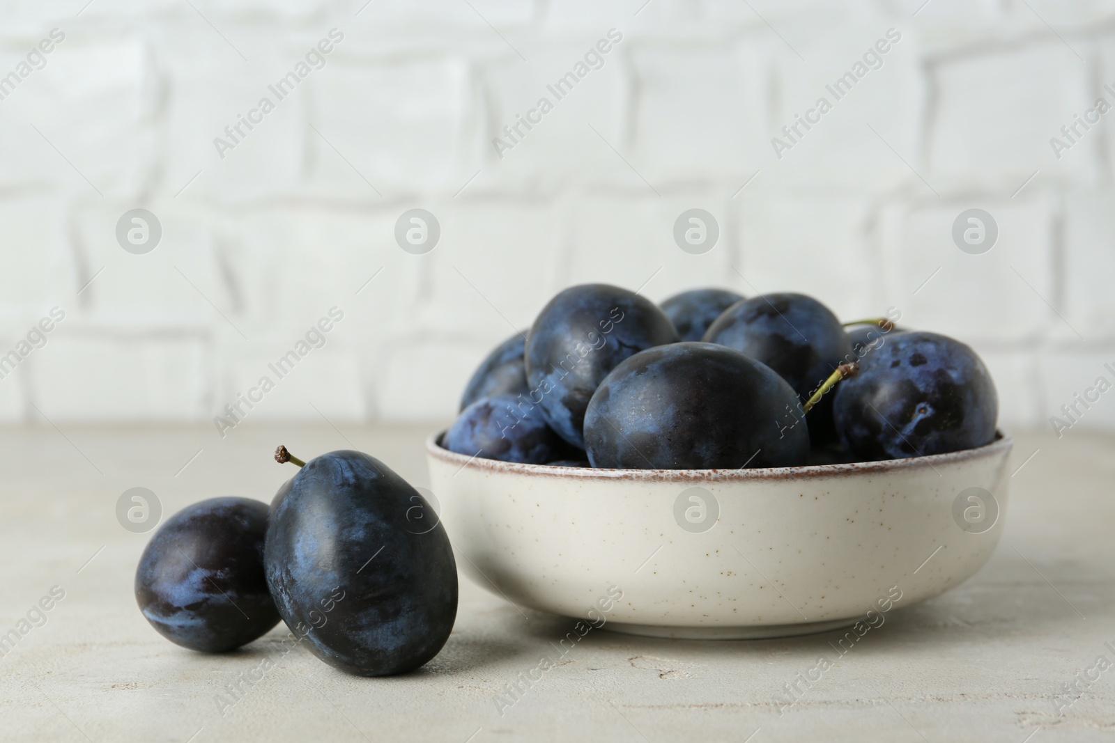 Photo of Ripe plums in bowl on light textured table, closeup