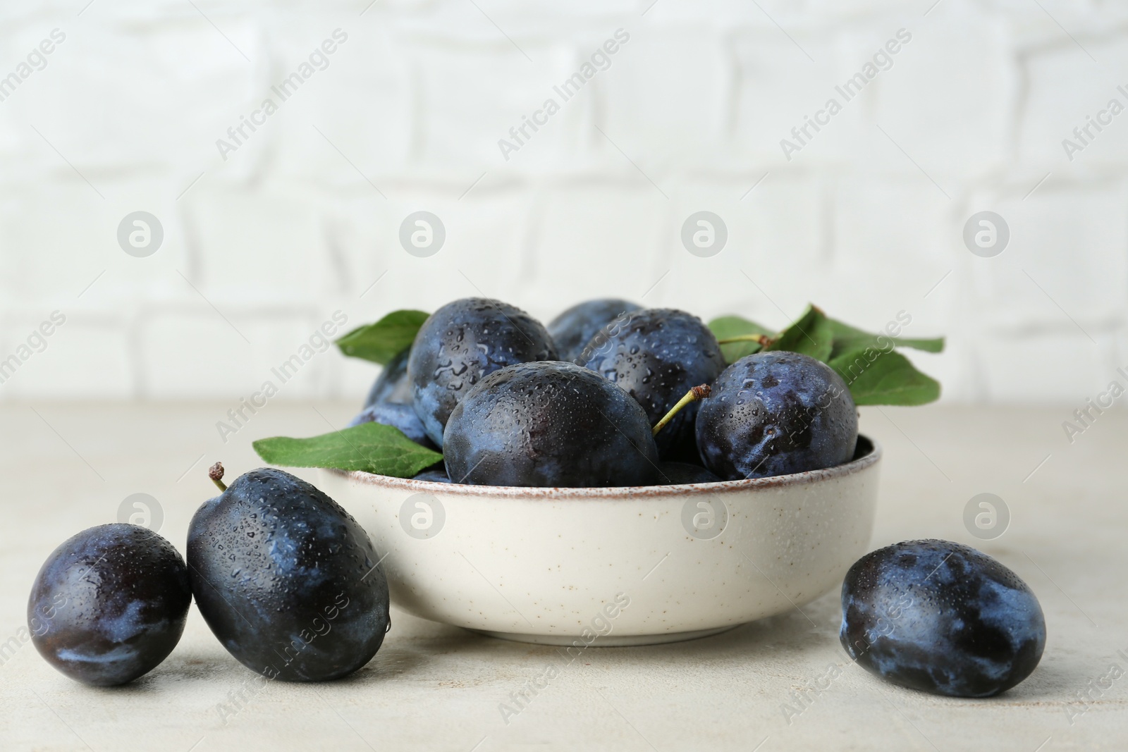 Photo of Ripe plums in bowl on light textured table, closeup