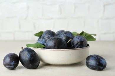 Photo of Ripe plums in bowl on light textured table, closeup