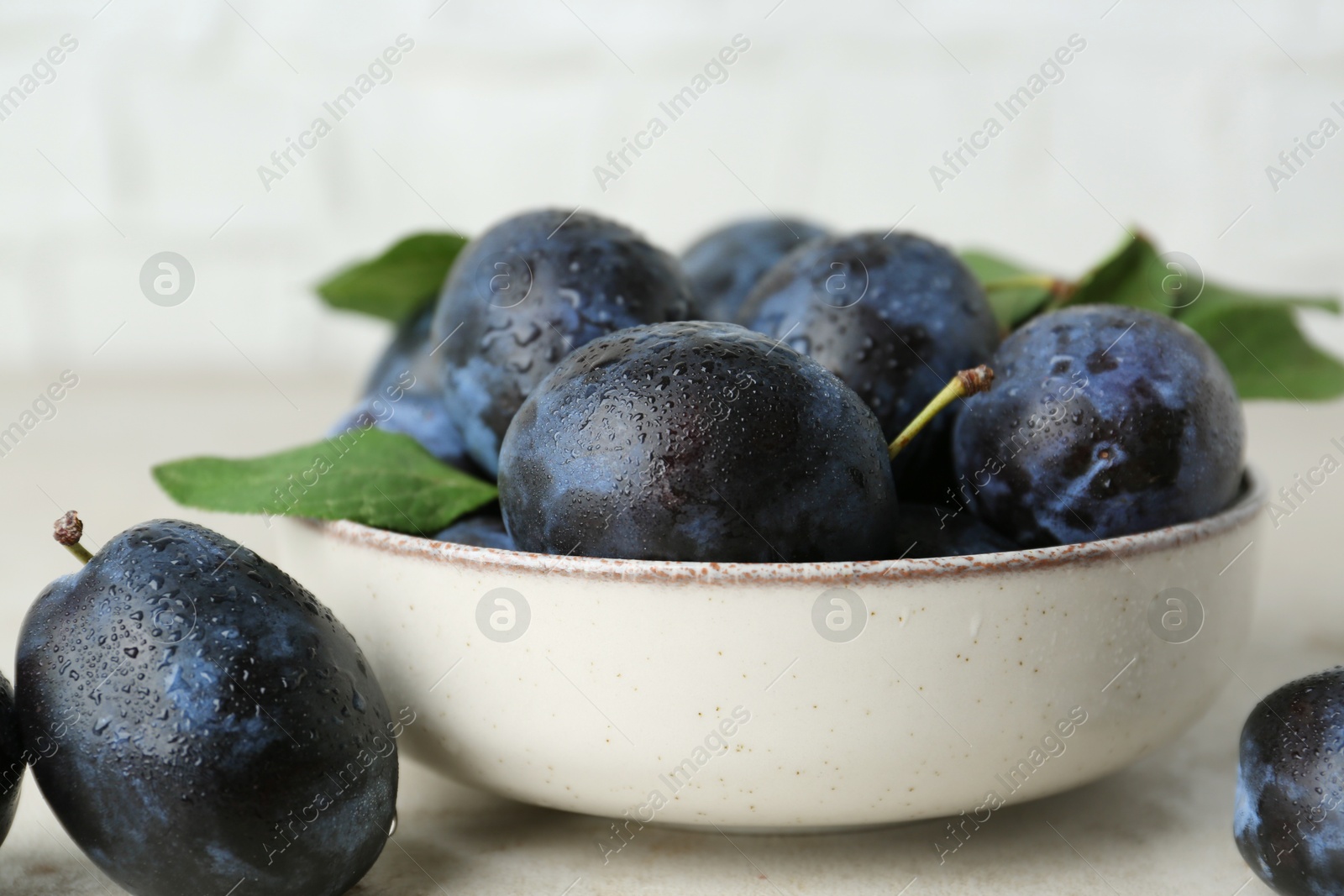 Photo of Ripe plums in bowl on light table, closeup