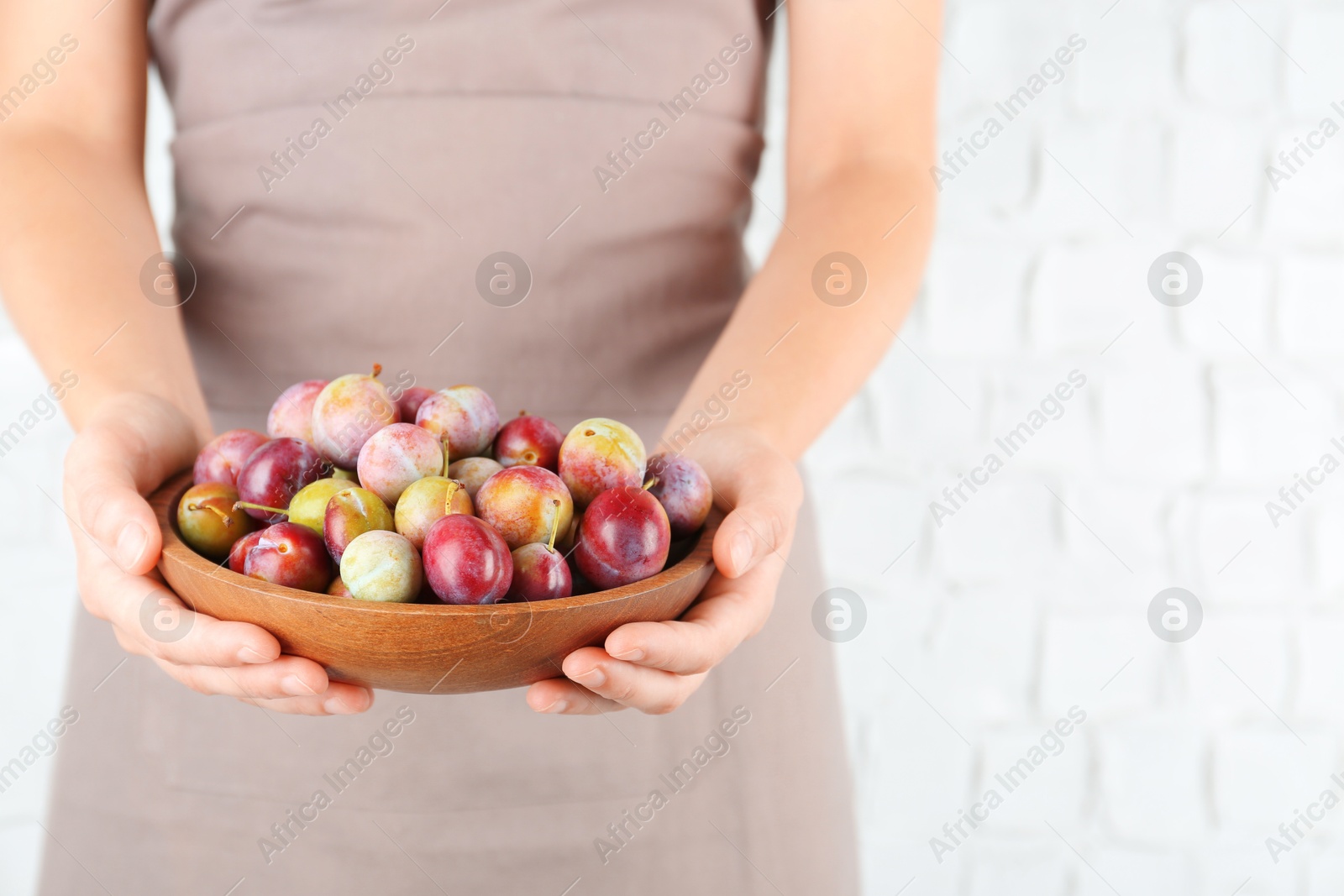 Photo of Woman holding bowl of ripe plums against white background, closeup