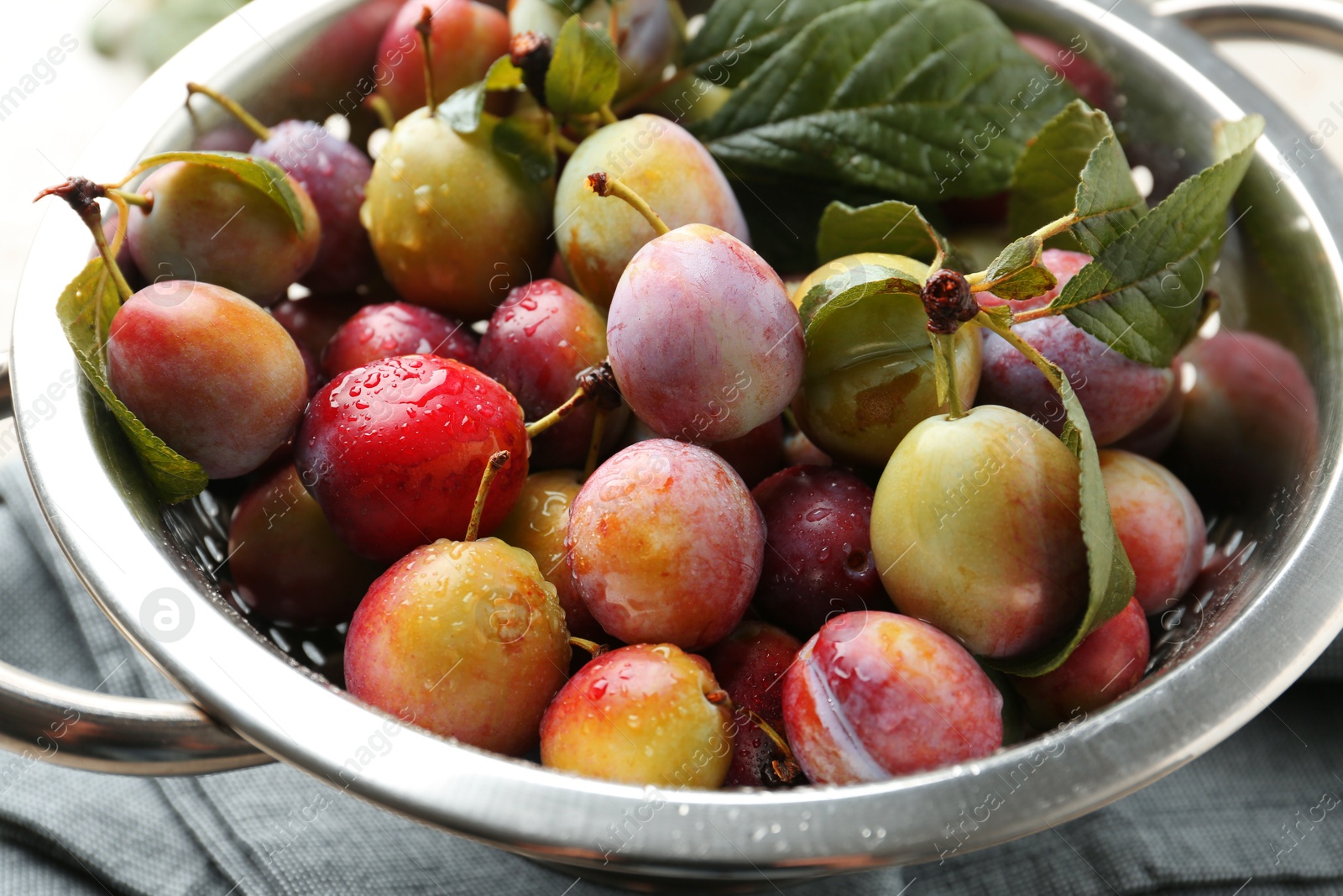 Photo of Ripe plums and leaves in colander on table, closeup