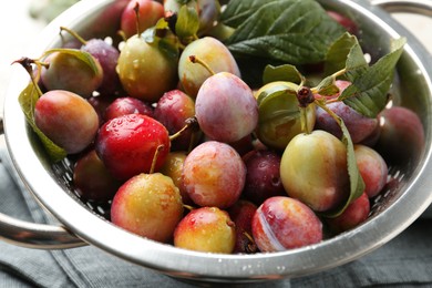 Photo of Ripe plums and leaves in colander on table, closeup