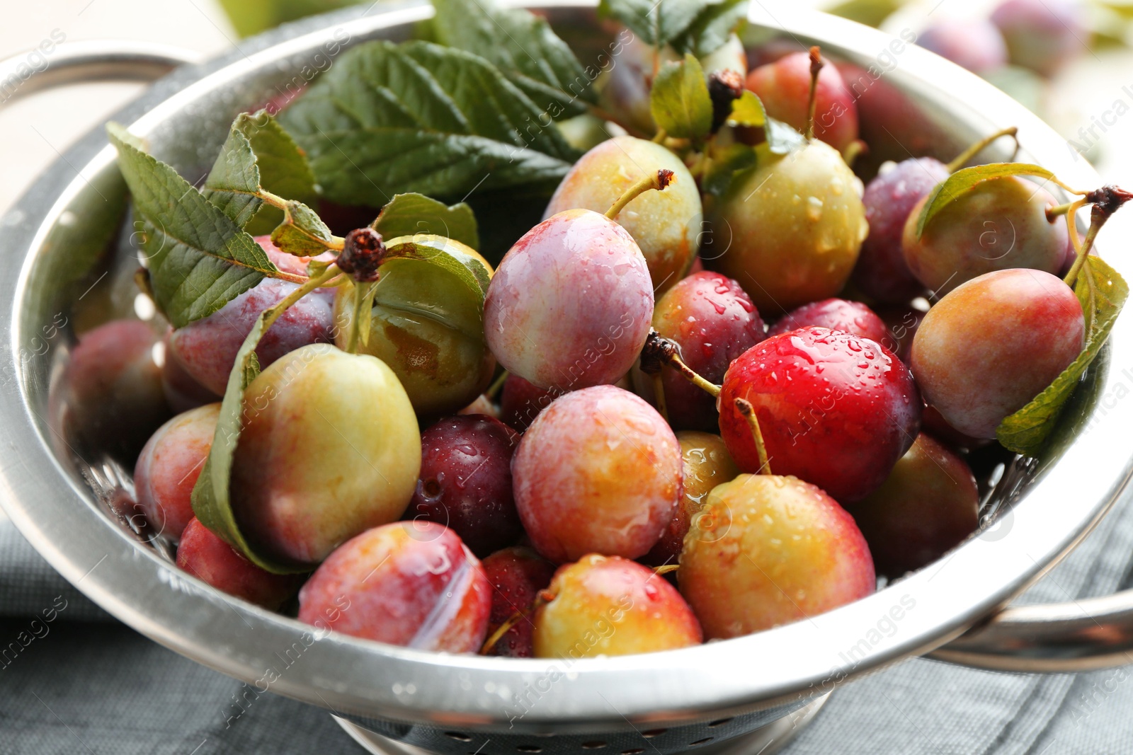 Photo of Ripe plums and leaves in colander on table, closeup