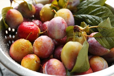 Photo of Ripe plums and leaves in colander on table, closeup