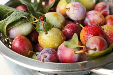 Photo of Ripe plums and leaves in colander on table, closeup