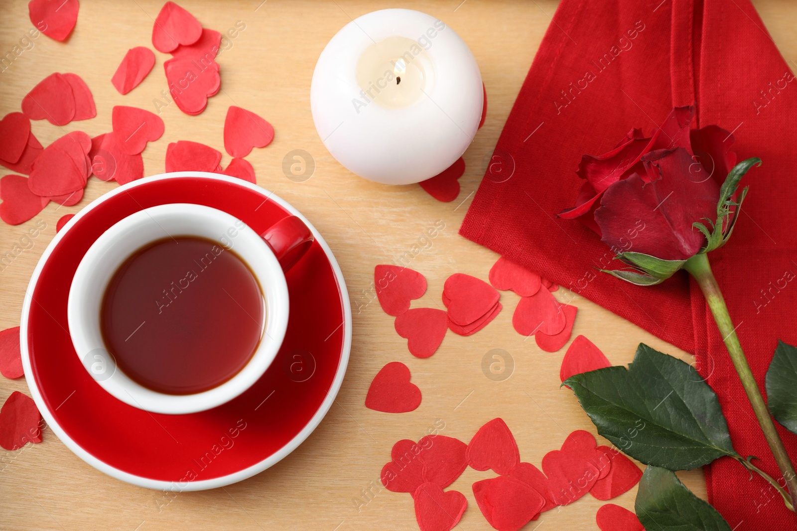 Photo of Burning candle, cup of tea, rose and red paper hearts on wooden table, flat lay