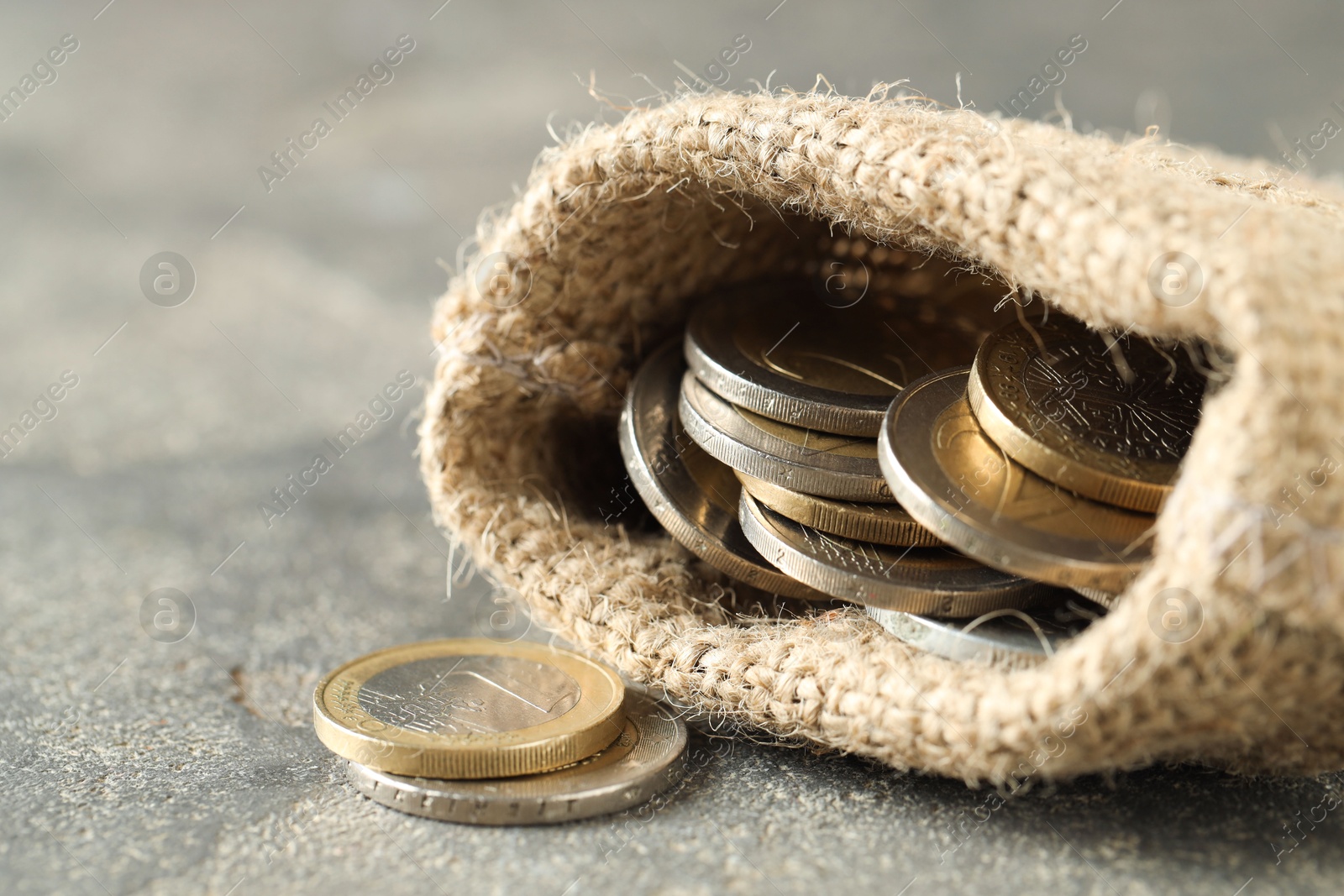 Photo of Euro coins in burlap sack on grey table, closeup