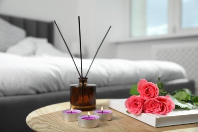 Photo of Burning candles, rose flowers, book and reed diffuser on wooden table indoors