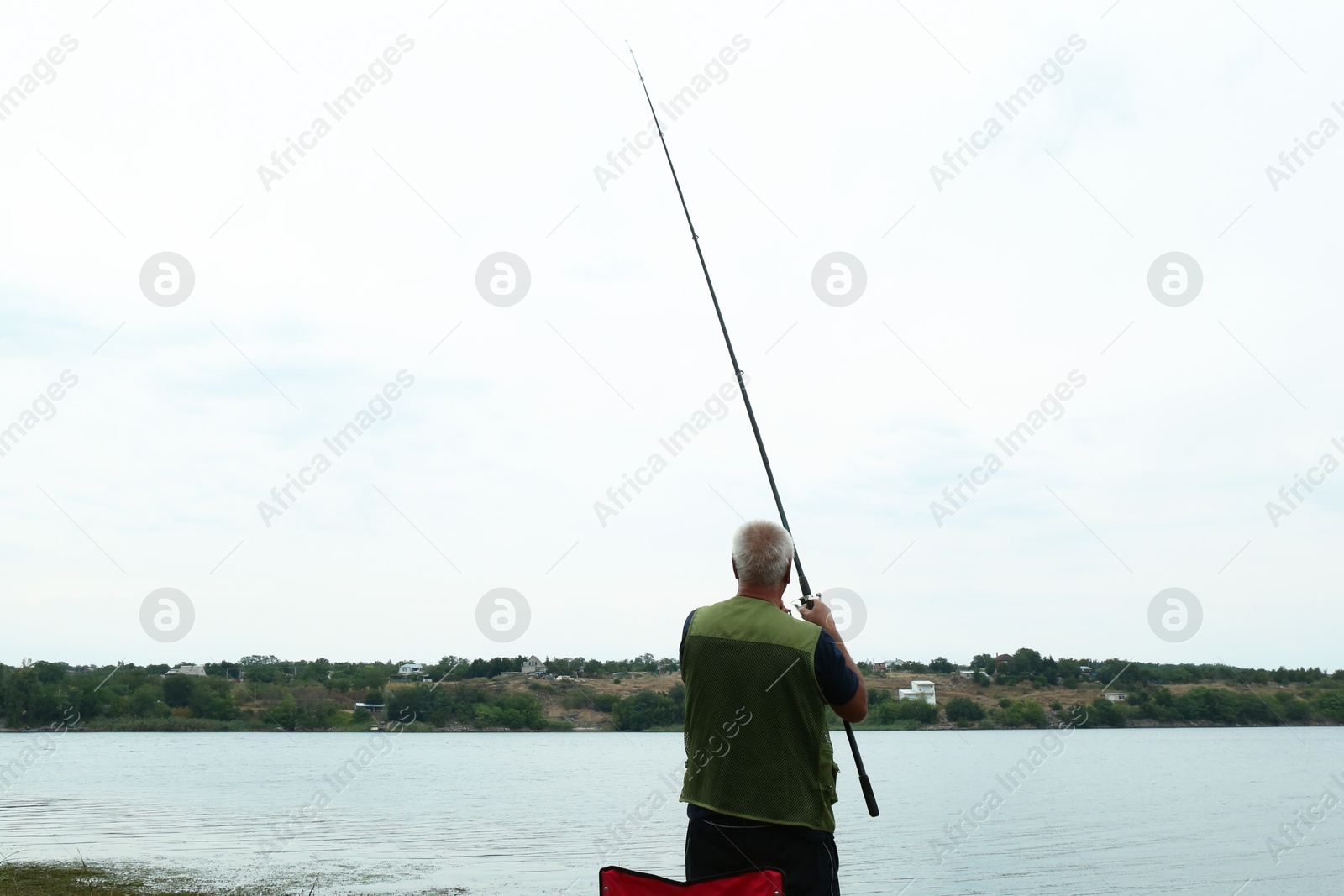 Photo of Fisherman with rod fishing near lake at summer, back view