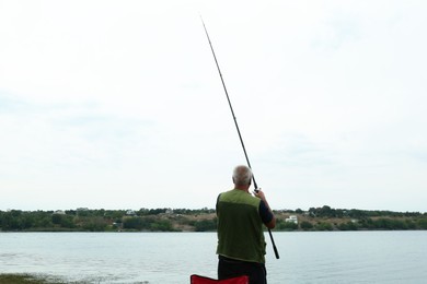 Fisherman with rod fishing near lake at summer, back view