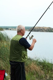 Fisherman with rod fishing near lake at summer