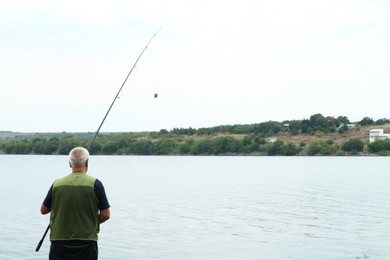 Photo of Fisherman with rod fishing near lake at summer, back view