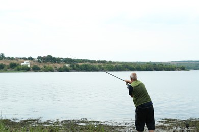 Photo of Fisherman with rod fishing near lake at summer, back view