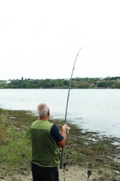 Photo of Fisherman with rod fishing near lake at summer, back view