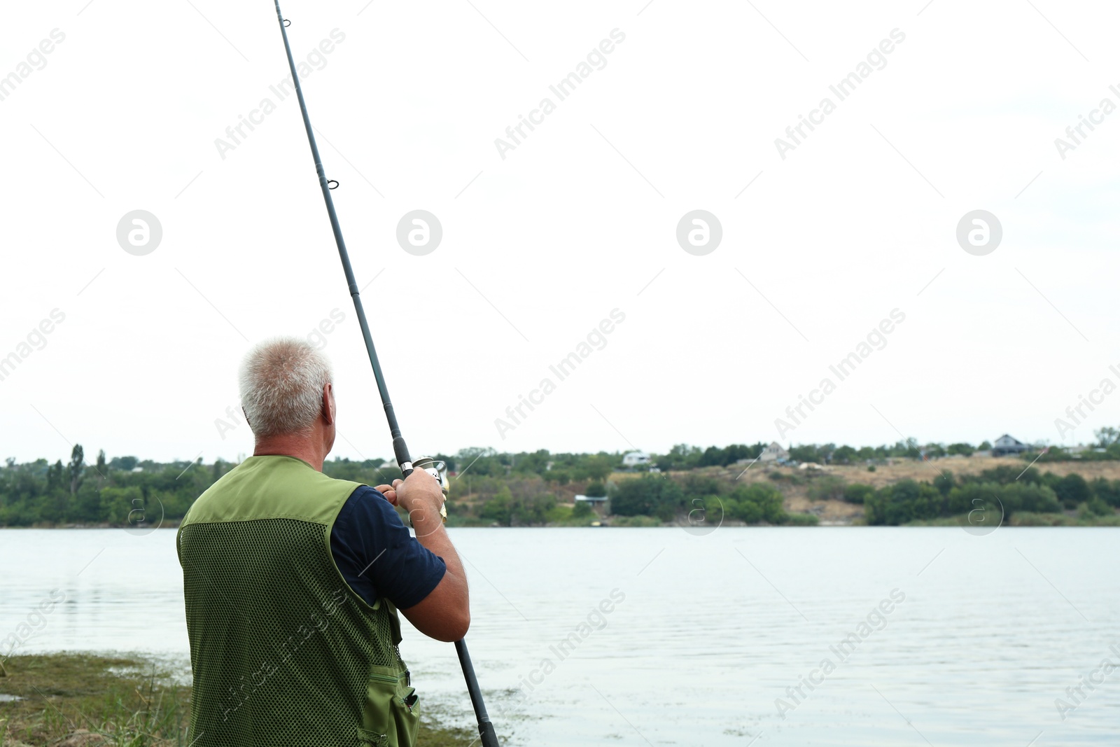 Photo of Fisherman with rod fishing near lake at summer, back view