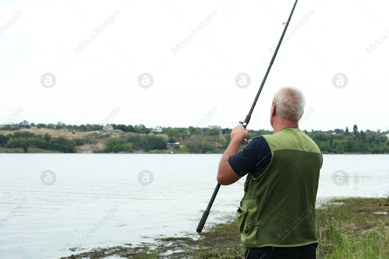 Photo of Fisherman with rod fishing near lake at summer, back view