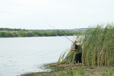 Photo of Fisherman with rod fishing near lake at summer